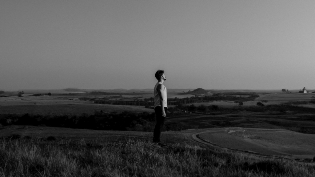 Homem de lado em um campo olhando pro horizonte