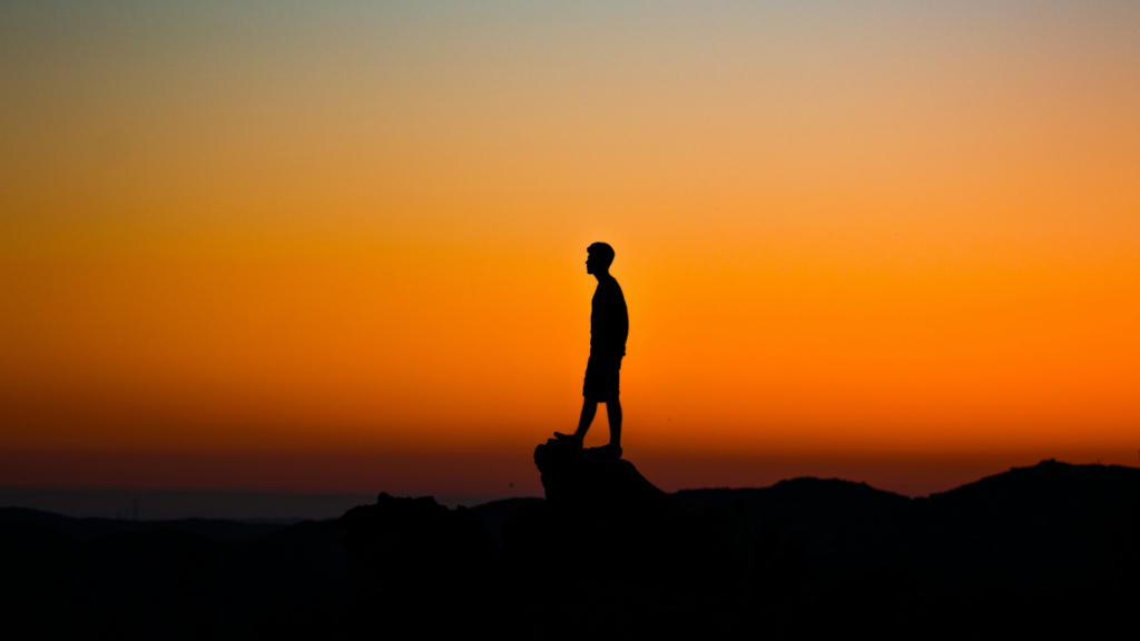 homem em silhueta no topo, com o céu alaranjado