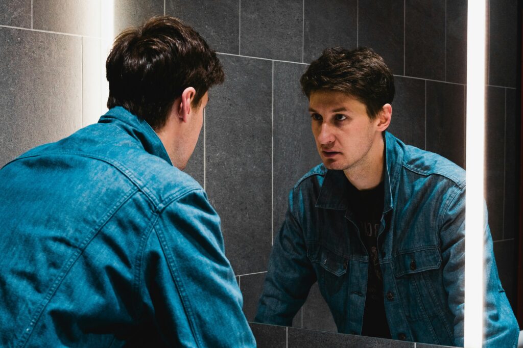 Um homem olhando fixamente para o próprio reflexo no espelho.