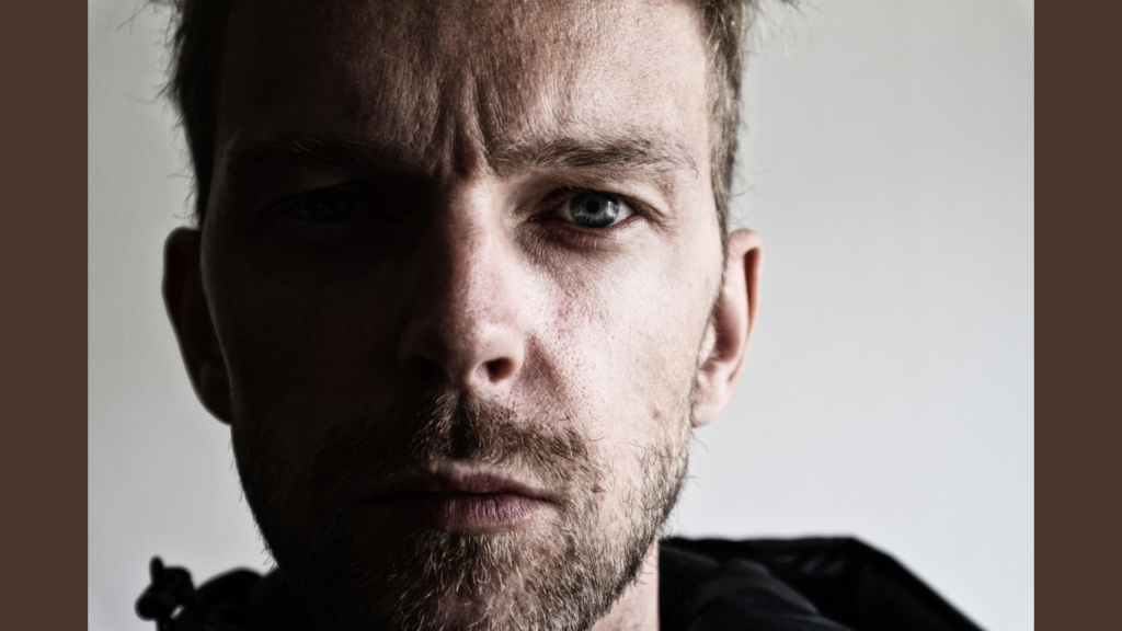 homem olhando pra frente, com um semblante sério e sombrio com metade do rosto na sombra